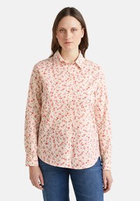 Blusa a maniche lunghe in tessuto rosa chiaro, con un motivo floreale caratterizzato da accenti rossi e verdi. Design con colletto, chiusura a bottoni e orlo curvo.