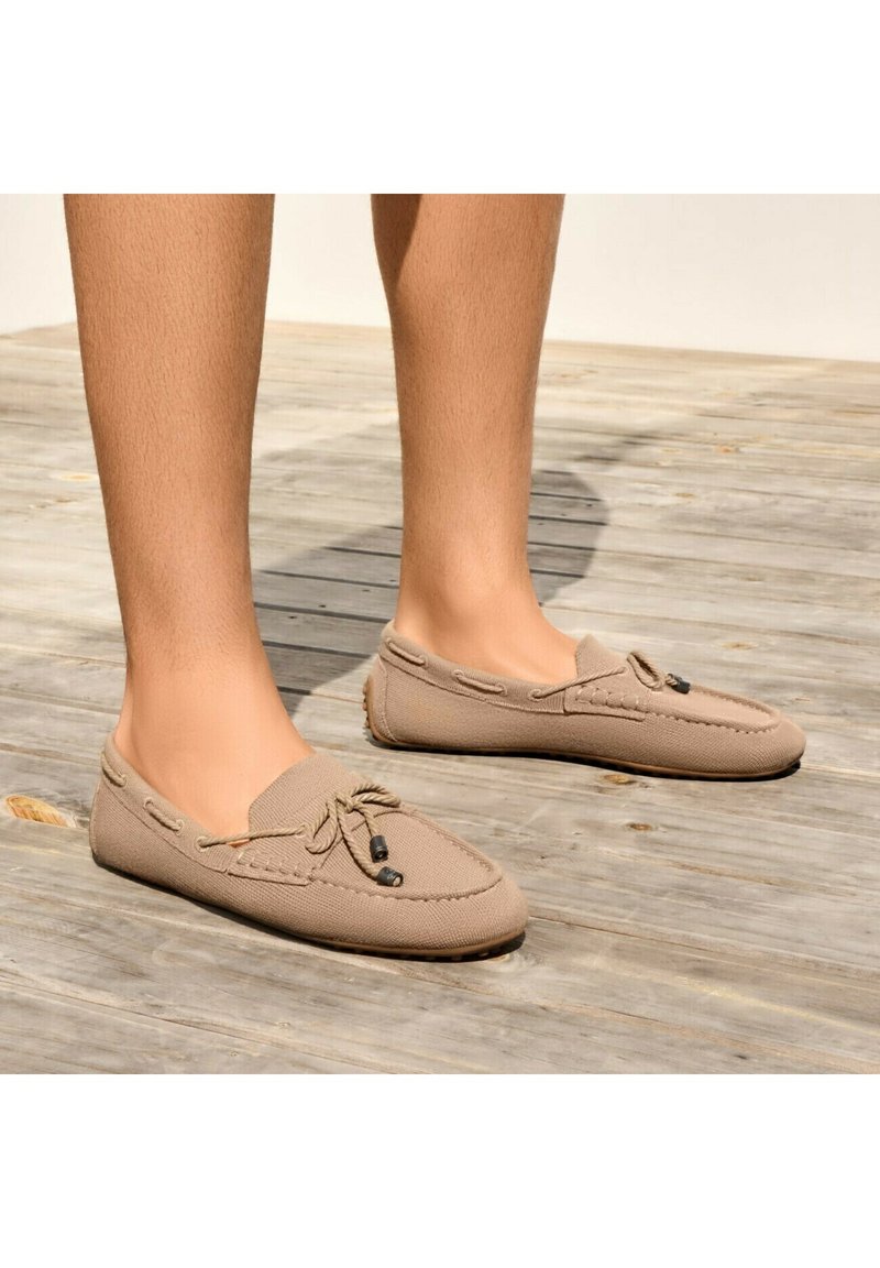 Beige Stoffslipper mit Gummisohlen, verziert mit gestickten Akzenten und einer dekorativen Schnürung. Glatte Oberfläche mit einem runden Zehendesign.