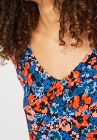 Květinová blůza s výstřihem do V, s černým pozadím a barevnými květinami v červených, modrých a růžových tónech. Měkká textura látky.