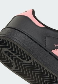 Crne i ružičaste tenisice s teksturiranom kožnom gornjom strukturom, gumeni potplat s cik-cak uzorkom i glatkim, zaobljenim dizajnom sa bočnim brendiranjem.