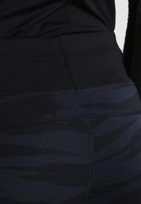 Vysoké legíny černé barvy s náměstcovým proužkováním ve stylu tygra, vyrobené z elastického materiálu. Disponují plochými švy pro větší komfort.