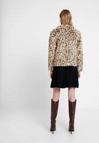 Tekoturkki, jossa on täpläinen kuvio beigen ja ruskean sävyissä, päällä musta laineileva hame, yhdistettynä polvenkorkuisiin ruskeisiin nahkasaappaisiin.