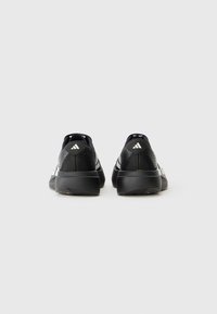 Baskets de sport noires avec un dessus texturé, des rayures blanches, des accents sur la languette du talon et une épaisse semelle noire. Vue arrière mettant en avant les détails de conception.