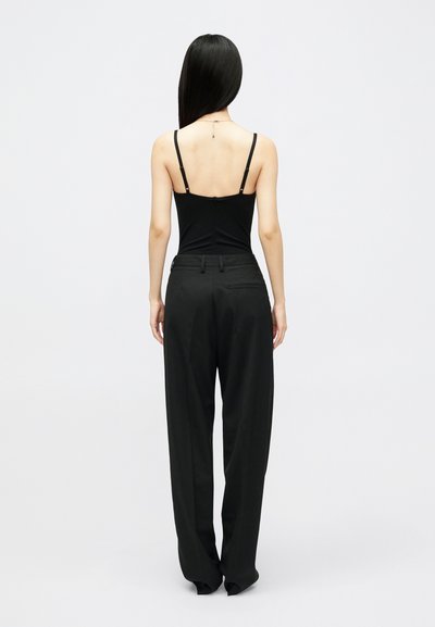 Must mustriga mustriga õhuke rihmad ja sobiva disainiga must kampsun, koos kõrge vöökohtadega mustade pükstega, esitleb minimalistlikku esteetikat.