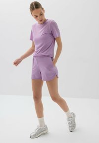 Fioletowa bluzka z krótkim rękawem i pasujące szorty, wykonane z lekkiej tkaniny. Posiada boczne kieszenie oraz luźny krój, dopełnione srebrnymi sneakersami.