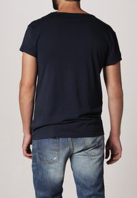 Granatowa bawełniana koszulka z okrągłym dekoltem i krótkimi rękawami, widoczna z tyłu, w połączeniu z wyblakłymi niebieskimi dżinsami.