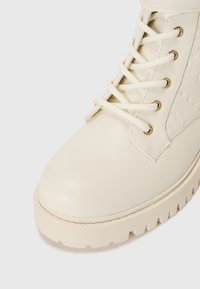 Stivaletto color beige chiaro realizzato in pelle liscia. Presenta punta arrotondata, suola piatta con bordo testurizzato e allacciatura frontale con occhielli in tono oro.
