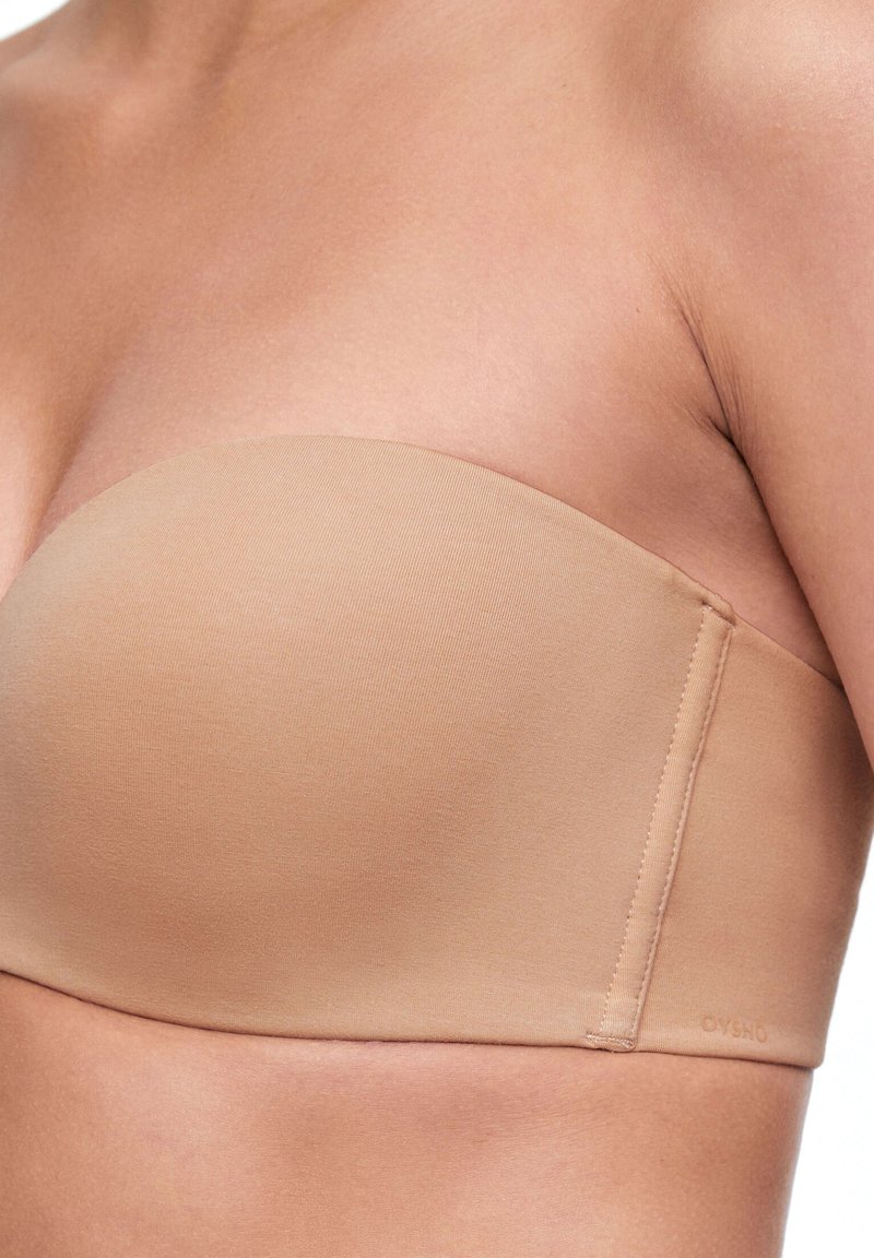 Soutien-gorge sans bretelles beige en tissu lisse, présentant une forme arrondie et des détails de couture minimaux, adapté à un port polyvalent.