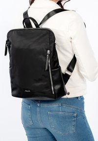 Mochila negra de nailon con textura suave, bolsillos con cremallera y correas ajustables. Presenta un diseño minimalista con acentos de hardware plateado.