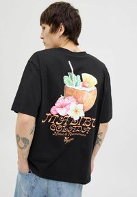 Mustat lyhythihaiset t-paidat, joissa on värikäs printti kookosjuomasta kukkien kanssa ja teksti "MALIBU COLADA" selkäpuolella.