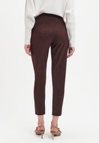 Brązowe, dopasowane spodnie z miękkiego, zamszowego materiału, z wysokim stanem i zwężanymi nogawkami, w połączeniu z beżowymi sandałami na obcasie.