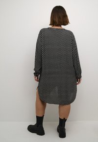 Blouse à motifs noir et blanc avec manches longues, ourlet arrondi, fentes latérales et coupe décontractée, associée à des bottines noires et des chaussettes.