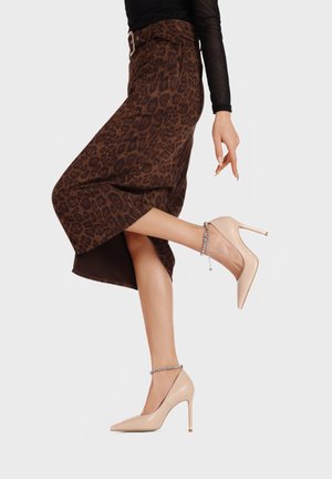 Gonna a metà lunghezza con stampa leopardata in tonalità marroni, con vita cintata, abbinata a scarpe con tacco nude e cinturino di strass alla caviglia.