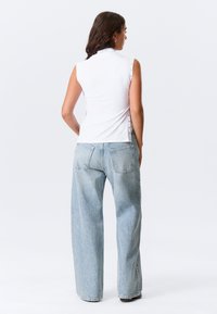 Λευκό αμάνικο τοπ με ψηλό λαιμόκοψη; τζιν παντελόνι με χαλαρή εφαρμογή και ανοιχτόχρωμο πλύσιμο; το τοπ διαθέτει πλευρικά κλείστρα για ρυθμιζόμενη εφαρμογή.