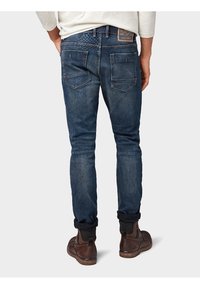 Pantalones vaqueros de mezclilla azul oscuro para hombre con corte ajustado, que cuentan con un diseño clásico de cinco bolsillos y costuras visibles en los bolsillos traseros.