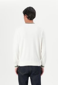Hvit strikket genser med rund hals, som har grønne, røde og hvite striper på mansjettene, båret med mørke denimjeans.