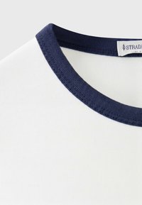 Close-up of white t-shirt neckline with navy blue ribbed collar and a partially visible clothing label.