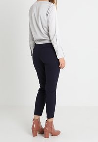 Blusa a maniche lunghe grigia chiara abbinata a pantaloni slim-fit blu navy e stivaletti rosa con texture lucida e tacco largo.