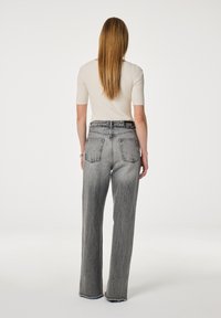 Grijze wijde jeans met een vervaagd uiterlijk en rafelige zoom, gecombineerd met een ribbelige crèmekleurige top. Bevat twee achterzakken en een hoge taille.