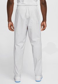 Calças cinzentas claras com uma cintura elástica e um bolso traseiro; textura suave com pernas ajustadas e punhos elásticos nos tornozelos.