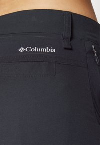 Calças Columbia pretas com uma textura suave, apresentando um bolso com fecho lateral e um logótipo bordado na cintura.