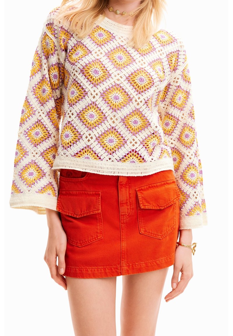 Pull en crochet avec un motif en losanges violet et jaune, associé à une jupe en jean orange vif avec des poches à l'avant.