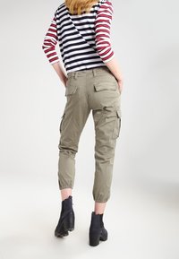 Khaki cargobroeken met tapse manchetten, zijzakken en een verstelbare taille, gecombineerd met een zwart-rode gestreepte lange mouwen top.
