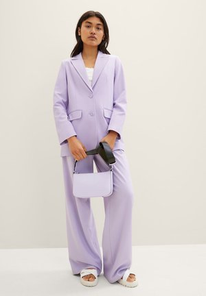Lavendelkleurige blazer en wijdvallende broek van lichtgewicht stof, met voorzakken en twee knopen. Houdt een kleine lavendelkleurige handtas met een zwarte schouderband vast.