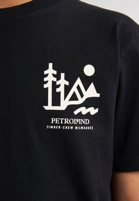 Černé bavlněné tričko s bílým grafickým designem stromů, hor a slunce, s textem "PETROLIND TIMBER-CREW MILWAUKEE" níže.