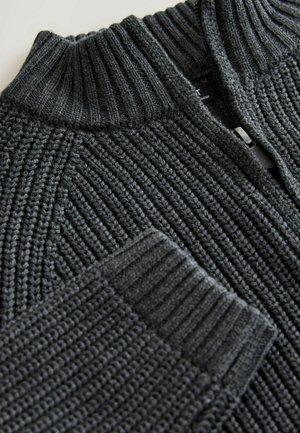 Dzianinowy, ciemnoszary sweter z wysokim prążkowanym kołnierzem, zamkiem błyskawicznym i teksturowanym wzorem z pionowym prążkowaniem. Miękki materiał.