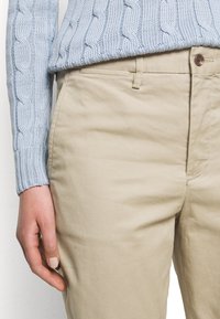 Světle modrý svetr s pleteným vzorem přes béžové bavlněné chinos kalhoty, s knoflíkovým zapínáním a bočními kapsami, má hladký povrch.