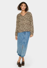 Blúzka s leopardím vzorom z ľahkého materiálu, kombinovaná s džínsovou midi sukňou s predným rozparkom. Hnedé mokasíny dopĺňajú outfit.