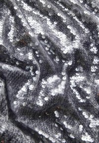 Czarna tkanina pokryta srebrnymi cekinami, o fakturowanym splocie. Cekiny odbijają światło, tworząc migoczący efekt na powierzchni.