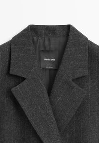 Mørkegrå uldfrakke med et hakket revers, en subtil stribet tekstur og en mærkat med "Massimo Dutti"-mærke inde i kraven.