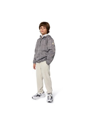 Veste coupe-vent avec un motif géométrique, en tons de gris et de blanc, dotée d'une capuche, d'une fermeture éclair et de poignets élastiques, associée à un pantalon léger et des baskets.