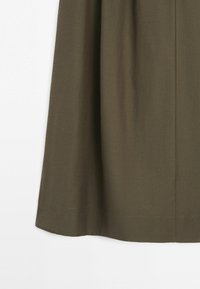 Nederste del af en olivengrøn nederdel med glat stof og en let udvidelse, vist mod en hvid baggrund.