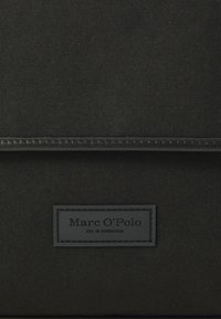 Borsa in tessuto nero con superficie liscia, leggero lucido e patch logo in rilievo con il testo "Marc O'Polo" e "EST. IN STOCKHOLM".