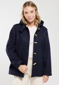 Giacca di lana navy con cappuccio, dotata di asole in legno, tasca trapuntata e vestibilità morbida. Tessuto liscio, maniche sartoriali.