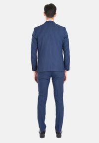 Completo blu navy con righe verticali, realizzato in lana, con una fessura centrale sul retro e pantaloni slim-fit, completato con scarpe eleganti nere.