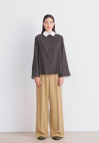 Brown striped button-up top with a white collar, paired with beige wide-leg trousers and dark green shoes. Plain background.