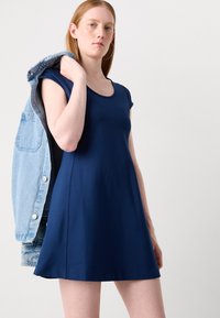 Navy blue short-sleeve dress with a round neckline and flared skirt. Denim jacket draped over the shoulder, showcasing a casual style.