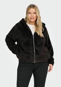 Must musta zip-up kapuutsiga, millel on pehme tekstuur ning elastsed mansetid ja äär. Kandmisel heledat särki ja musti pükse.