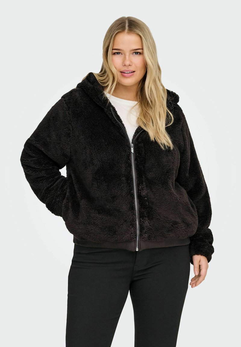 Must musta zip-up kapuutsiga, millel on pehme tekstuur ning elastsed mansetid ja äär. Kandmisel heledat särki ja musti pükse.