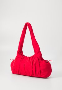 Sac à main rembourré rouge avec une texture douce et froissée. Dispose d'une large anse courbée et d'une fermeture éclair sur un côté. Forme compacte et arrondie.