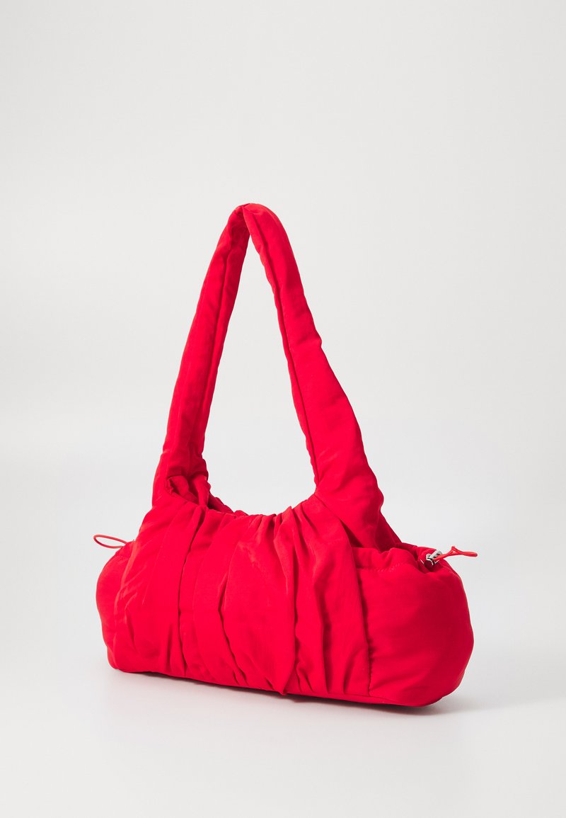 Bolso de mano acolchado rojo con una textura suave y arrugada. Presenta un asa ancha y curvada y un cierre de cremallera en un lado. Forma compacta y redondeada.
