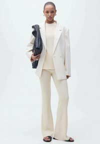 Creme striktrøje og flagrende bukser parret med en oversized hvid blazer. Holder en tekstureret sort taske. Glat stof, minimalisk design.