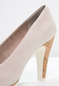 Chaussure à talon haut beige avec une tige en suède texturé, un talon en liège et une base blanche brillante, avec un design élégant et arrondi des orteils.