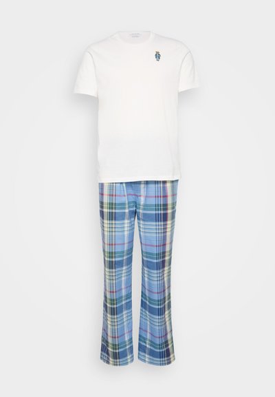 Balta īsām piedurknēm T-kreklā ar mazu zilu un brūnu izšūtu dizainu, saskaņota ar zilu ruļļu naktsbiksēm, kurās ir daudzkrāsainas līnijas.