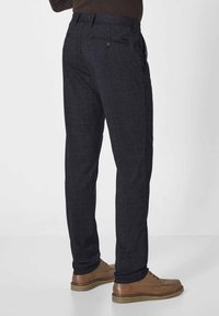 Navy plaid trousers made from textured fabric, featuring a back pocket with button closure and slim-fit design. Brown shoes complement the outfit.