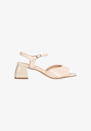 Sandalia beige de punta abierta con tacón de charol y una correa en el tobillo, que presenta una textura suave y un diseño curvado.